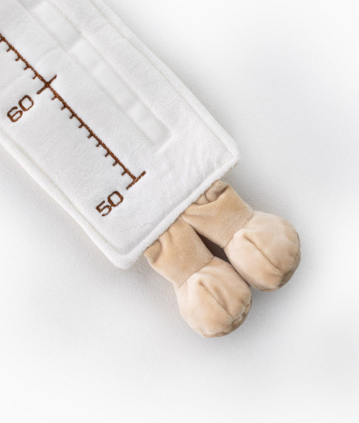 Close-up of white plush baby growth chart with embroidered brown numbers and soft beige bear feet detail