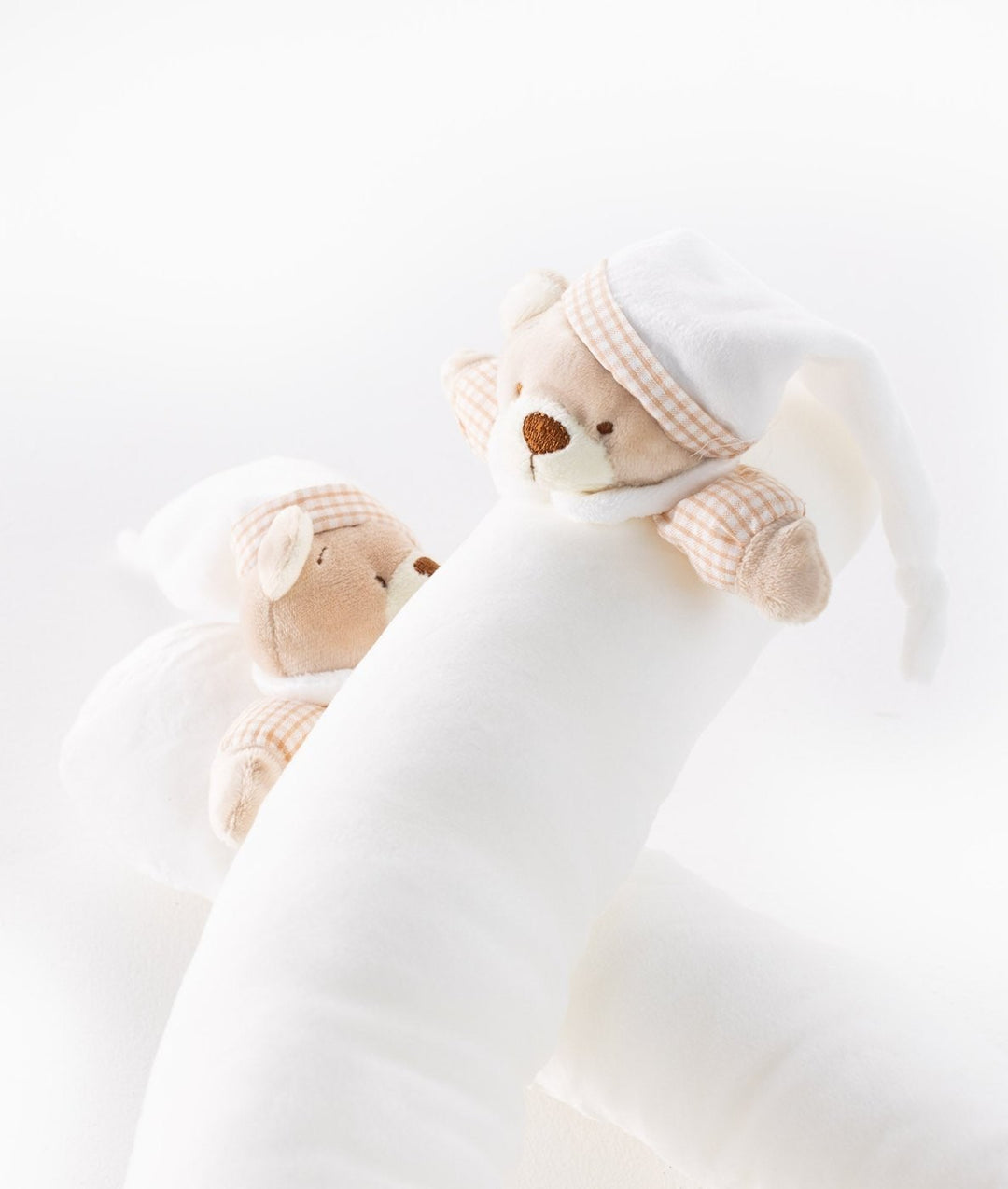 Angled view of white bolster with plush bears wearing gingham nightcaps