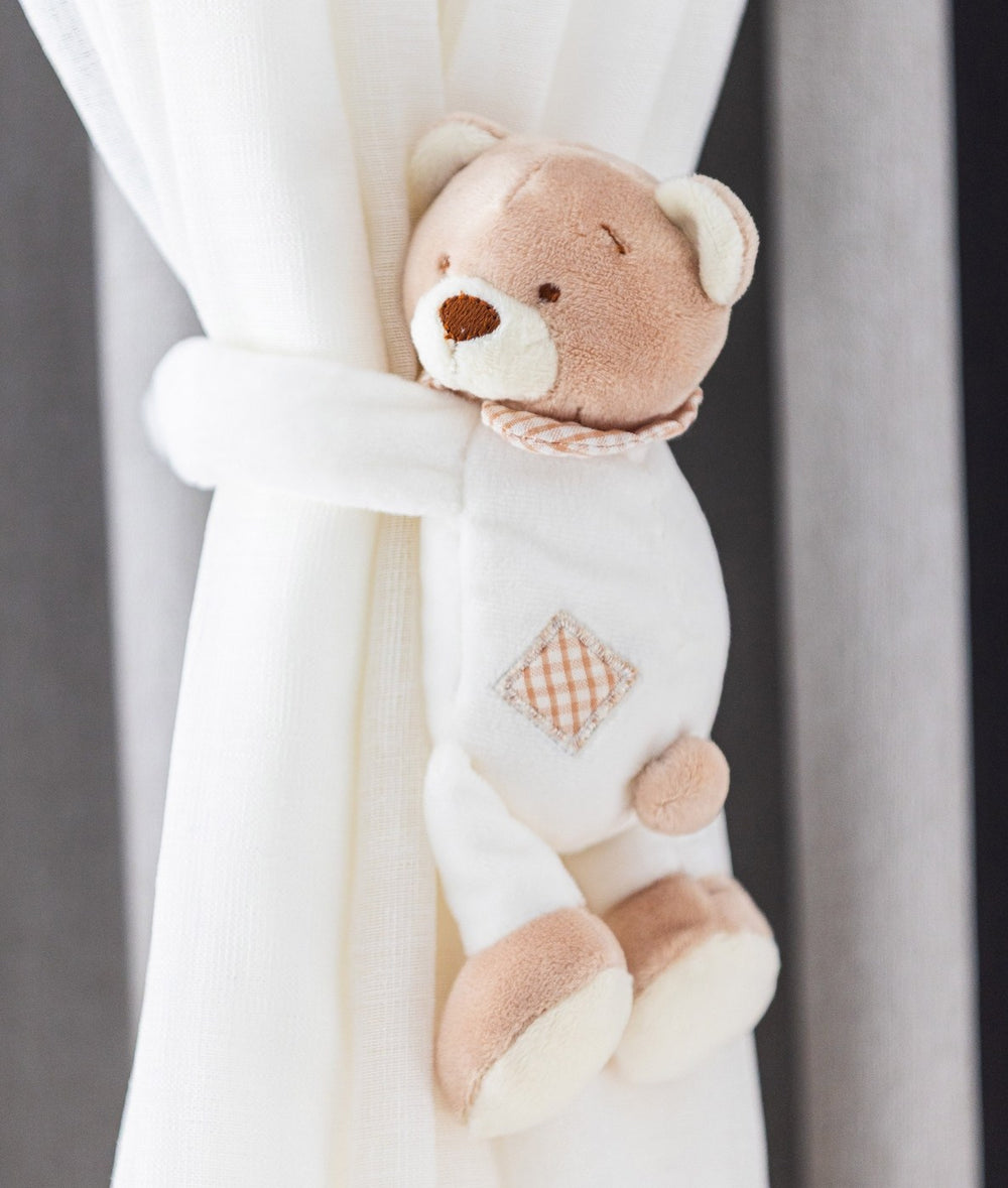 Beige and white plush teddy bear curtain tieback with embroidered face and gingham tummy holding sheer curtain