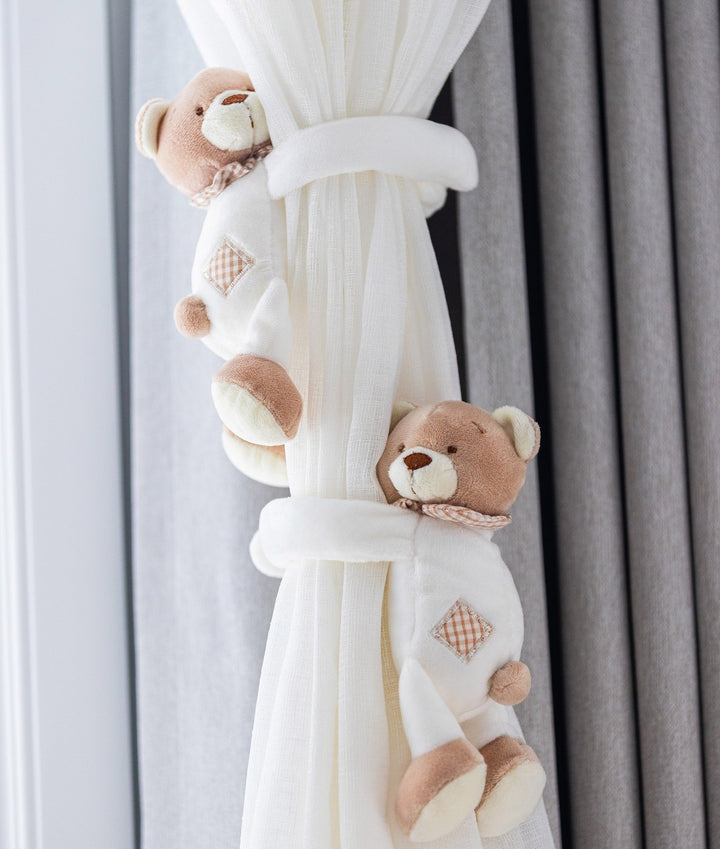 Bear curtain tieback securing white sheer panel against grey blackout curtain for nursery decor