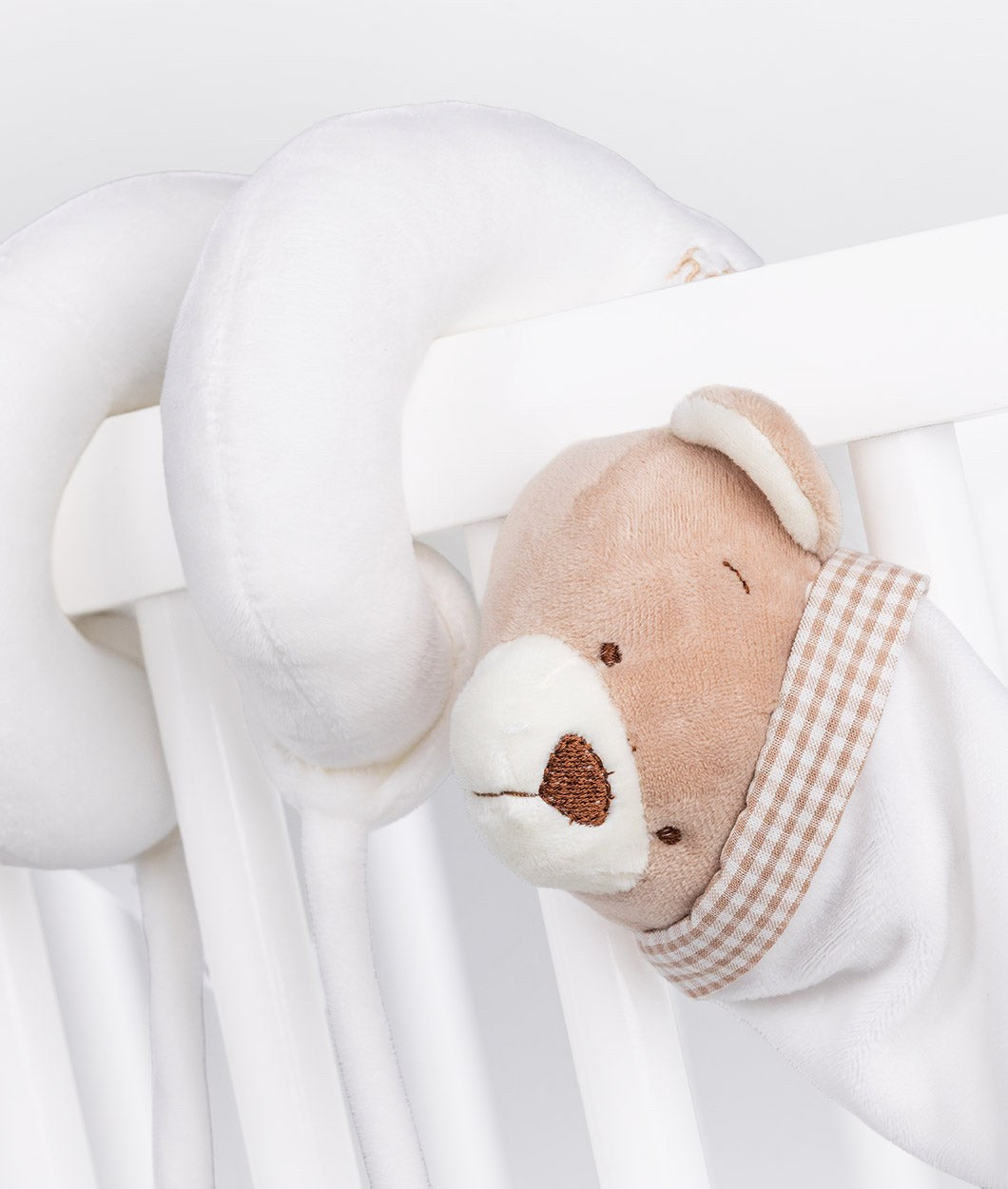 Beige and white bear spiral activity toy wrapped on cot rail with embroidered nose