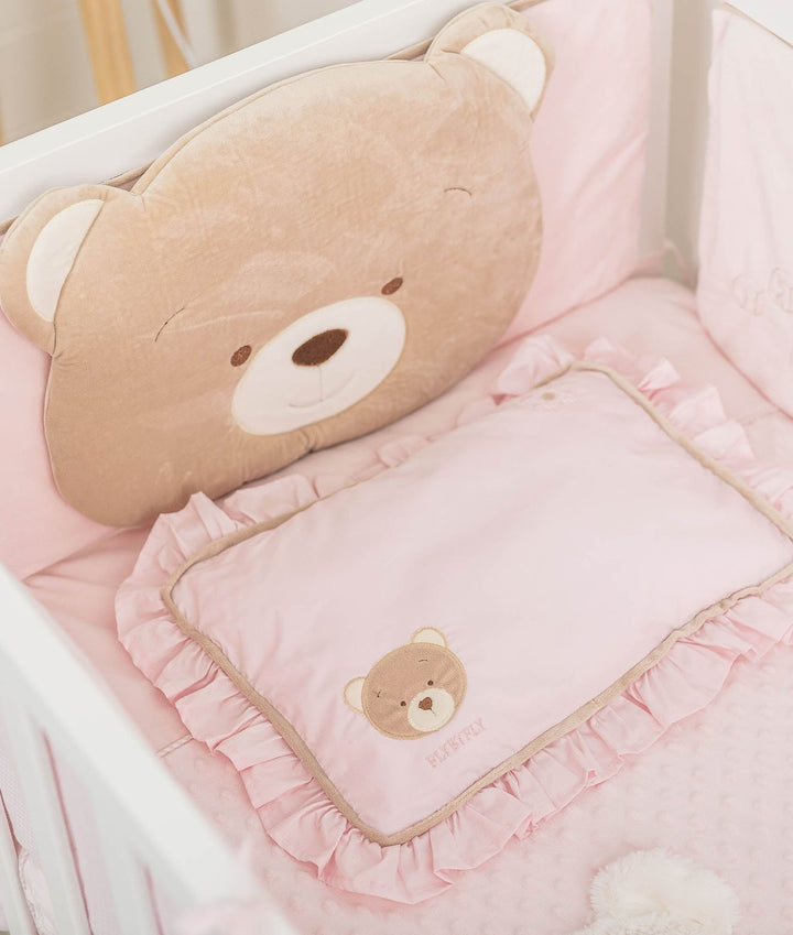 Cot arrangement with plush tan bear back cushion and ruffled pink pillow on dotted quilt