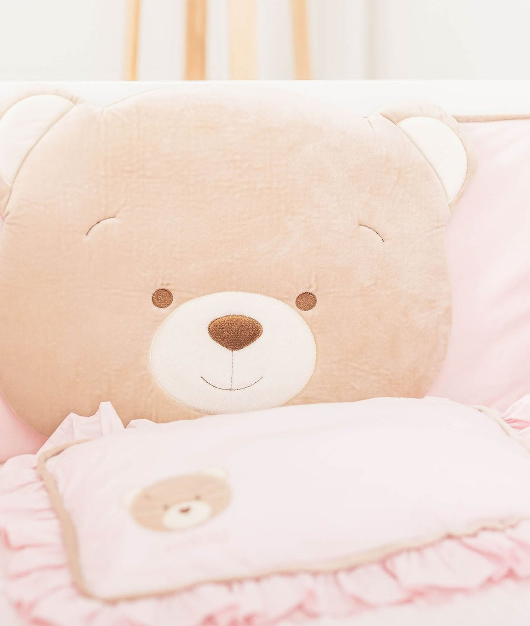 Soft velvety tan bear head cushion detail behind pink ruffled pillow with bear applique