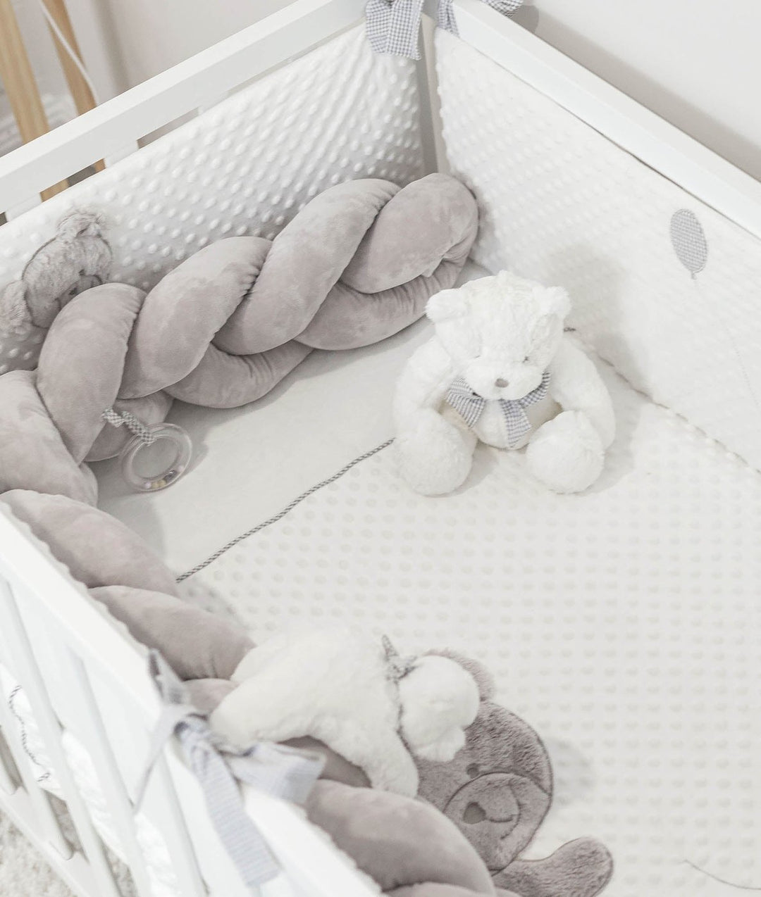 white dotted toddler bedding set with grey braided bumpers and bear applique
