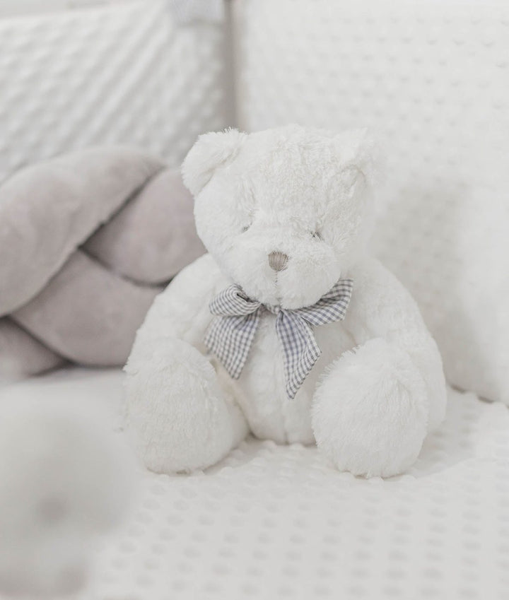 fluffy white teddy bear in grey checkered bow tie on dotted bedding