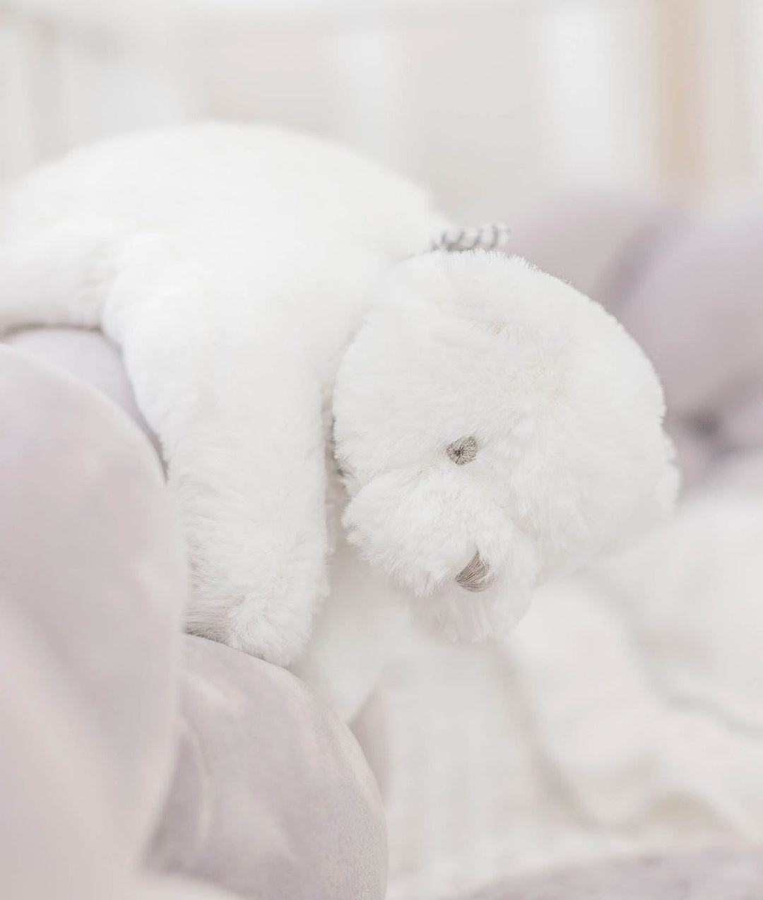 white plush teddy bear with silver sequin ear detail on grey velvet bedding