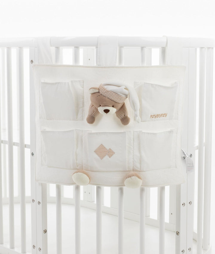 Cream colored hanging nursery storage caddy with multiple compartments and beige checkered trim mounted on white baby crib