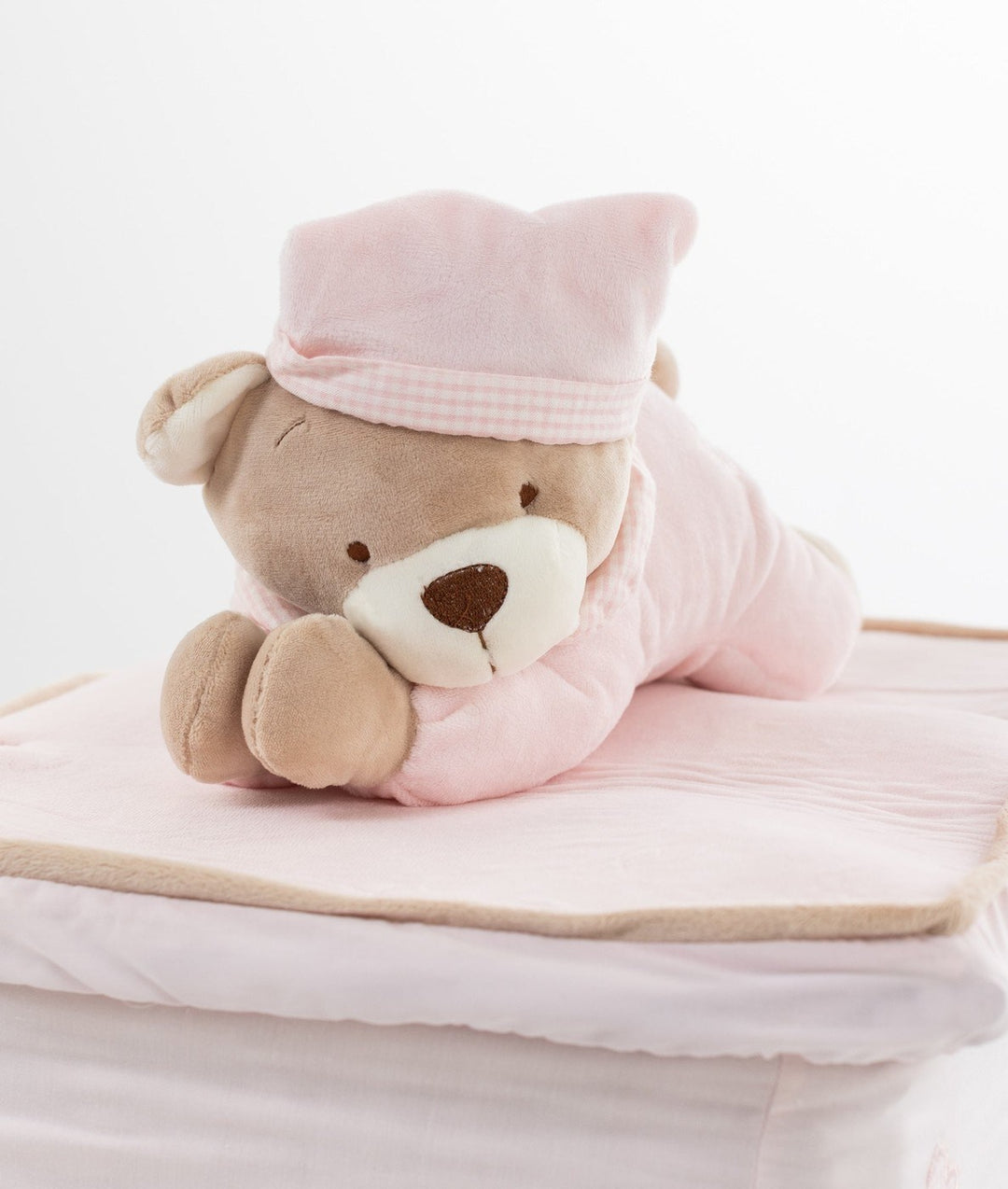Teddy bear in pink quilted onesie lying on soft padded wicker basket lid